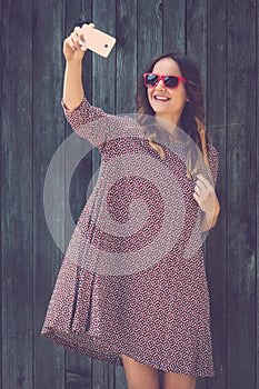 Young female taking selfie with smartphone against wooden wall