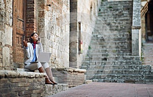 Young female talking on her cell phone with laptop, sitting outdoor on stairways in italy