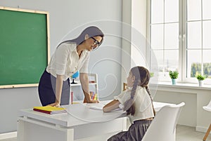Young female teacher and girl elementary school pupil talking in classroom photo