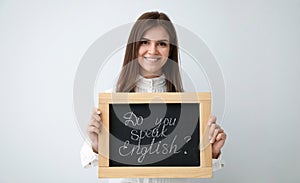 Young female teacher holding chalkboard with words DO YOU SPEAK ENGLISH? on light background