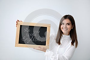 Young female teacher holding chalkboard with words DO YOU SPEAK ENGLISH? on light background