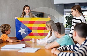 Young female teacher holding colorful flag of Estelada while working with preteens in classroom