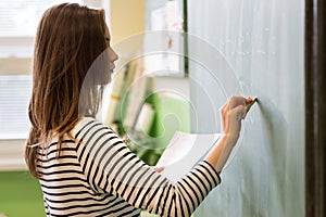 Young female teacher or a student writing math formula on blackboard. photo