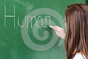 Young female teacher teaching in biology class. Teacher writing Human Body on blackboard.