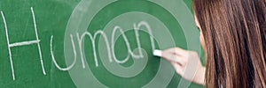 Young female teacher teaching in biology class. Teacher writing Human Body on blackboard using chalk.