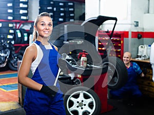 female technician standing with wheel balancing machinery at auto workshop