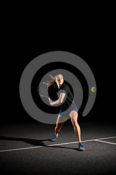 Young female tennis player with racket ready to hit yellow tennis ball.