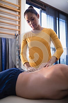 Young female therapist massaging back of senior male patient lying on bed