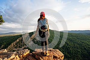 A young female tourist with a backpack admires the sunset from the top of the mountain. A traveler on the background of mountains