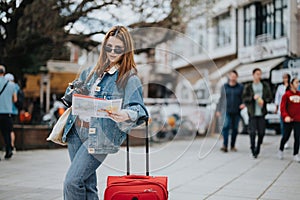 Young female tourist with camera and map exploring city on a sunny day