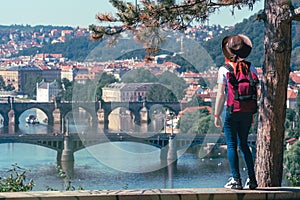 Young female tourist in a cowboy hat with sunglasses and a backpack, enjoying great view on the old town of Prague. Praha, Travel