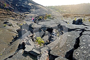 Young female tourist exploring surface of the Kilauea Iki volcano crater with crumbling lava rock in Volcanoes National Park in Bi
