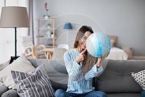 Young female tourist holding globe, pointing with index finger to desirable destination of her trip. Planning vacation