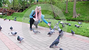a young female tourist with a large backpack and colorful hair feeds pigeons in a city park.