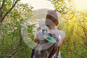Young female tourist with map in hand wanders through the forest. Back view. Light