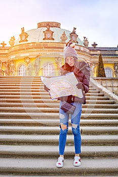 Young female tourist with map looking for a way to Sans Souci palace in Potsdam, Berlin, Germany, Europe