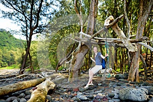 Young female tourist relaxing on a handmade swing on rocky beach of Pololu Valley on Big Island of Hawaii