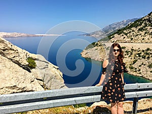 A young female tourist sitting along the railing at a highway stop along the adriatic highway in Croatia.