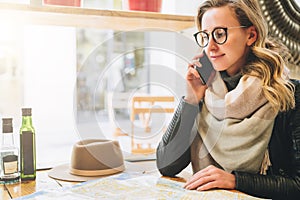 Young female tourist is sitting in cafe at table and talking on cell phone. Girl is calling her friend. Tourism, travel.