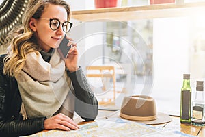 Young female tourist is sitting in cafe at table and talking on cell phone. Girl is calling her friend. Tourism, travel.