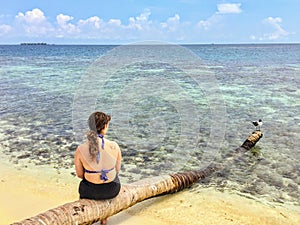 A young female tourist sitting on a log on the secluded remote tropical island of Laughing bird caye