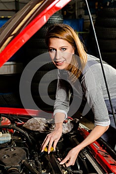 Young female trainee fixing car engine in garage