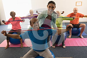 Young female trainer assisting senior man in fitness studio