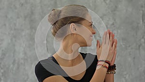 Young female trainer doing namaste pose and smiling, welcome group before yoga class