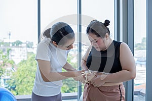 Young female trainer measuring fat layer of overweight woman with caliper at fitness