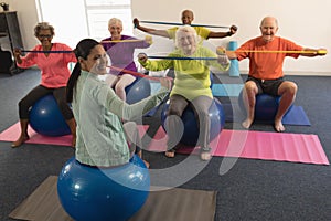 Young female trainer and senior people exercising with resistance band