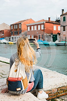 Young female traveler by the canal in Murano in Venice, Italy taking a photo