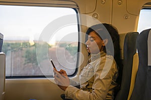 Young female traveler enjoying travel with her smartphone. Cute young girl traveling with classic train sitting near the window