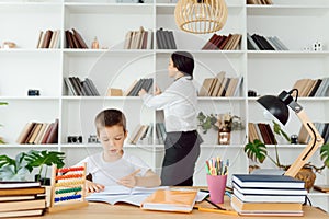 Young female tutor helping little elementary school boy with homework during individual lesson at home