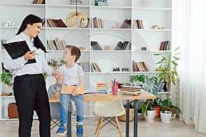 Young female tutor helping little elementary school boy with homework during individual lesson at home