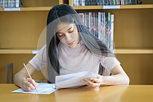 Young female university student concentrate doing language practice examination inside library