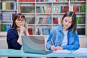 Female university student with teacher preparing for exam, inside library