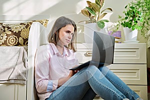 Young female university student studying at home sitting on floor using laptop