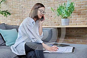 Young female university student studying at home, talking on cell phone