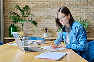 Young female university student studying at home, using laptop