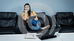 A young female university student uses tablet studying oline sits on couch at home. A teenager woman spends time during covid-19 p photo