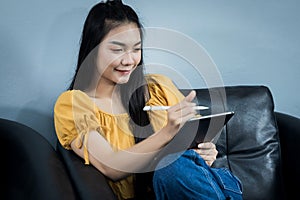 A young female university student uses tablet studying oline sits on couch at home. A teenager woman spends time during covid-19 p photo