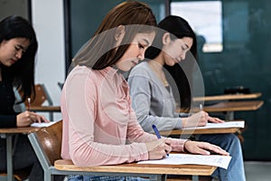 Young female university students concentrate on doing examination in classroom. Girl students seriousely writes the exercise of