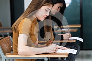 Young female university students concentrate on doing examination in classroom. Girl students seriousely writes the exercise of