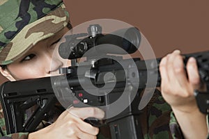 Young female US Marine Corps soldier aiming M4 assault rifle over brown background