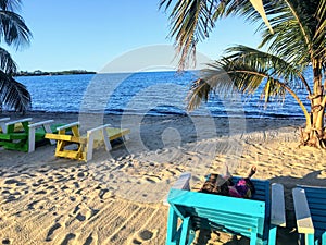 A young female vacationer relaxing in a beach chair along the sandy beaches of beautiful Placencia, Belize enjoying the sun.