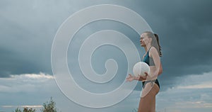 Young female volleyball player is serving ball at match of beach volleyball, medium shot, slow motion