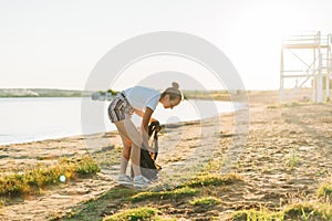 Young female volunteer satisfied with picking up trash, a plastic bottles and coffee cups, clean up beach with a sea