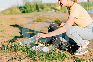 Young female volunteer satisfied with picking up trash, a plastic bottles and coffee cups, clean up beach with a sea