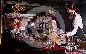 Young female waiter taking order from visitors in luxurious restaurant