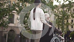 Young female on walk with disabled elderly male in wheelchair, family support